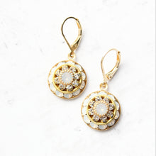 Load image into Gallery viewer, A pair of gold leverback drop earrings with circular floral designs, featuring white opal glass and clear rhinestone accents, displayed on a white background.