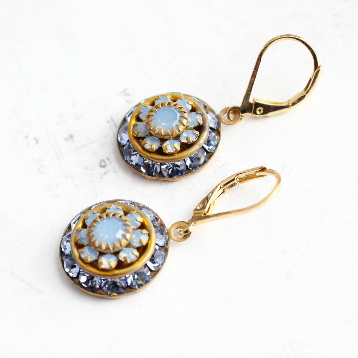 A pair of gold leverback drop earrings with circular blue and white floral designs, displayed on a light textured white background.