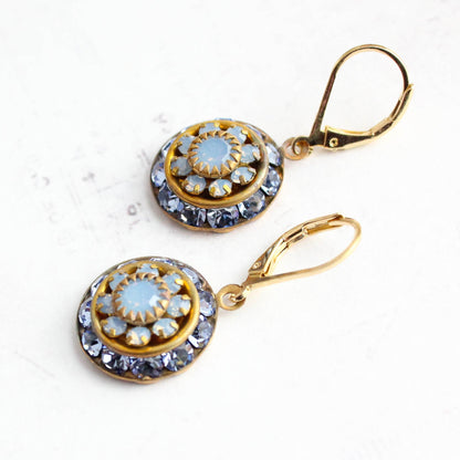 A pair of gold leverback drop earrings with circular blue and white floral designs, displayed on a light textured white background.