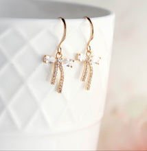 Load image into Gallery viewer, Gold bow-shaped earrings with clear stones on a white background