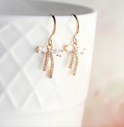 Gold bow-shaped earrings with clear stones on a white background