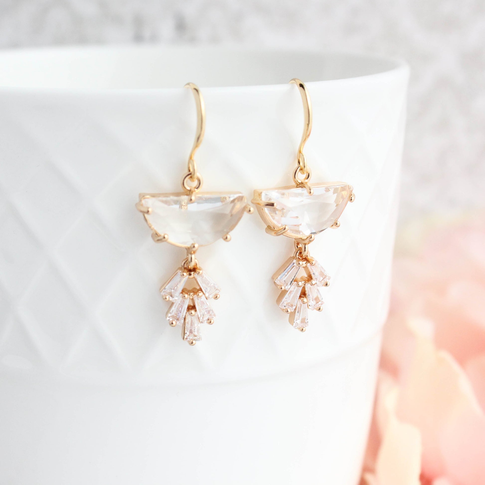 A pair of Art Deco style gold-plated dangle earrings with a half moon glass stone and a sparkling baguette multi-stone leaf design, displayed against a white background.