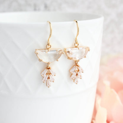 A pair of Art Deco style gold-plated dangle earrings with a half moon glass stone and a sparkling baguette multi-stone leaf design, displayed against a white background.