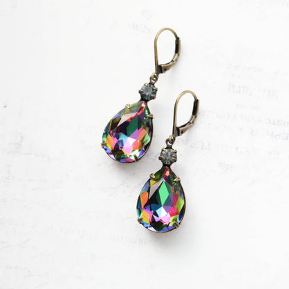 A pair of teardrop-shaped drop earrings with iridescent rainbow faceted crystals and antique bronze leverback hooks, displayed on a light textured white background.