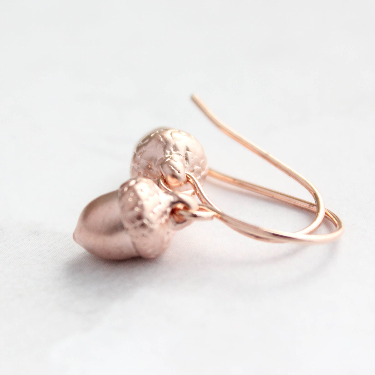 Rose gold acorn-shaped earrings on a light background