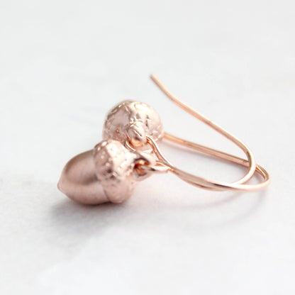 Rose gold acorn-shaped earrings on a light background