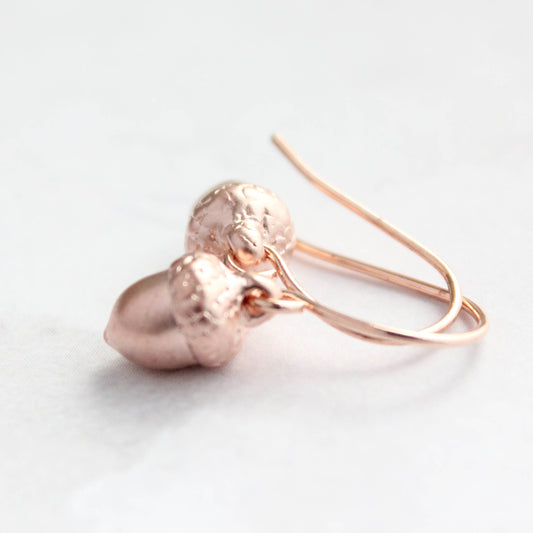 Rose gold acorn-shaped earrings on a light background