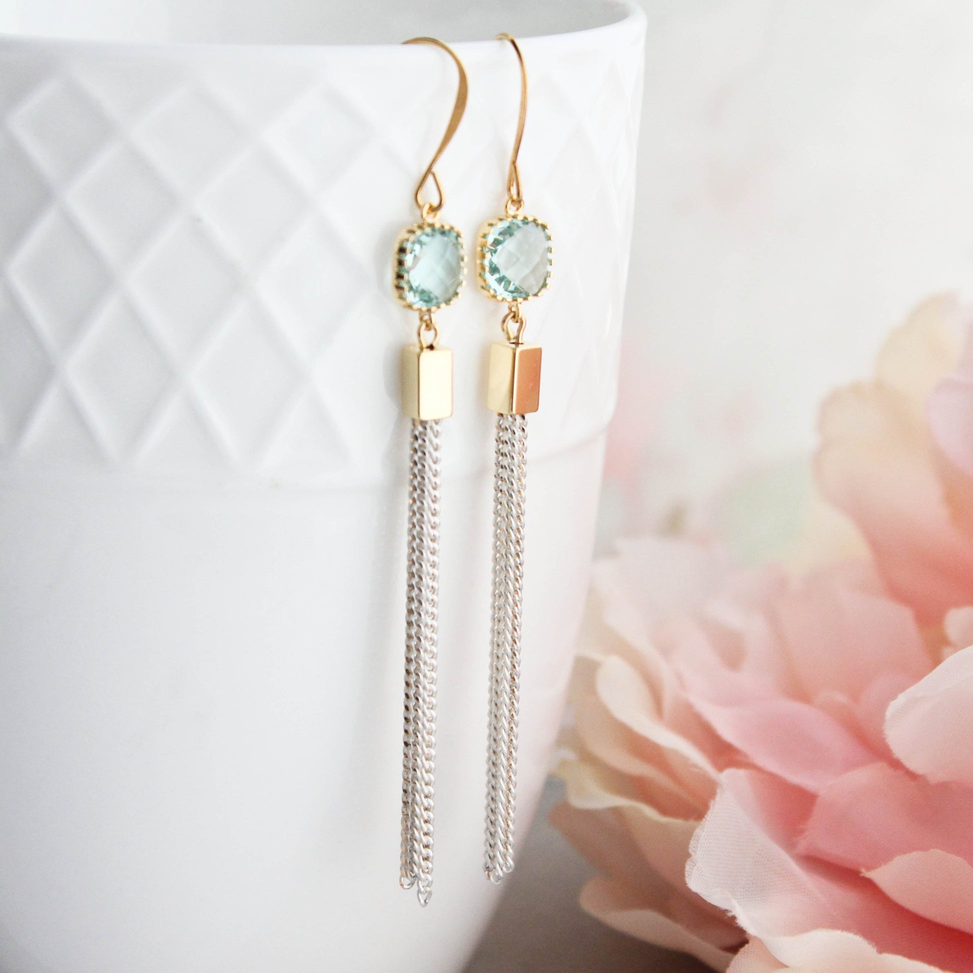 Long chain tassel earrings with aqua glass jewels and ivory gold chain, displayed hanging from a white cup.