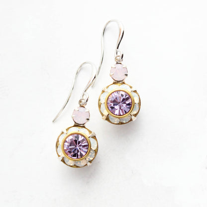 A pair of gold and silver drop earrings featuring a central round purple crystal surrounded by small white opal glass stones, with a smaller light pink crystal above, shown on a white background.