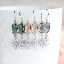 Load image into Gallery viewer, three pairs of dangling earrings displayed on a white textured ceramic cup. Each pair features a faceted oval top stone in green, blush pink, or smoky gray, suspended from silver hooks with leaf-shaped clear crystal drops.