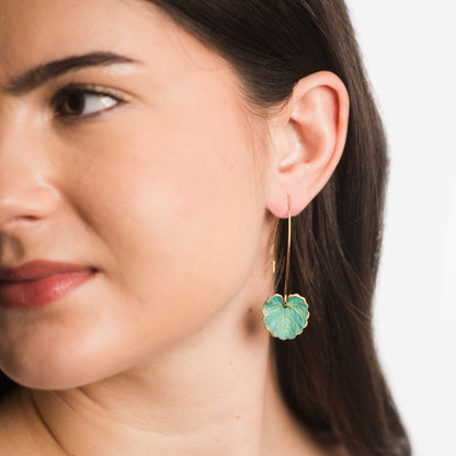 Close-up of a woman wearing green leaf-shaped earrings with a plain background