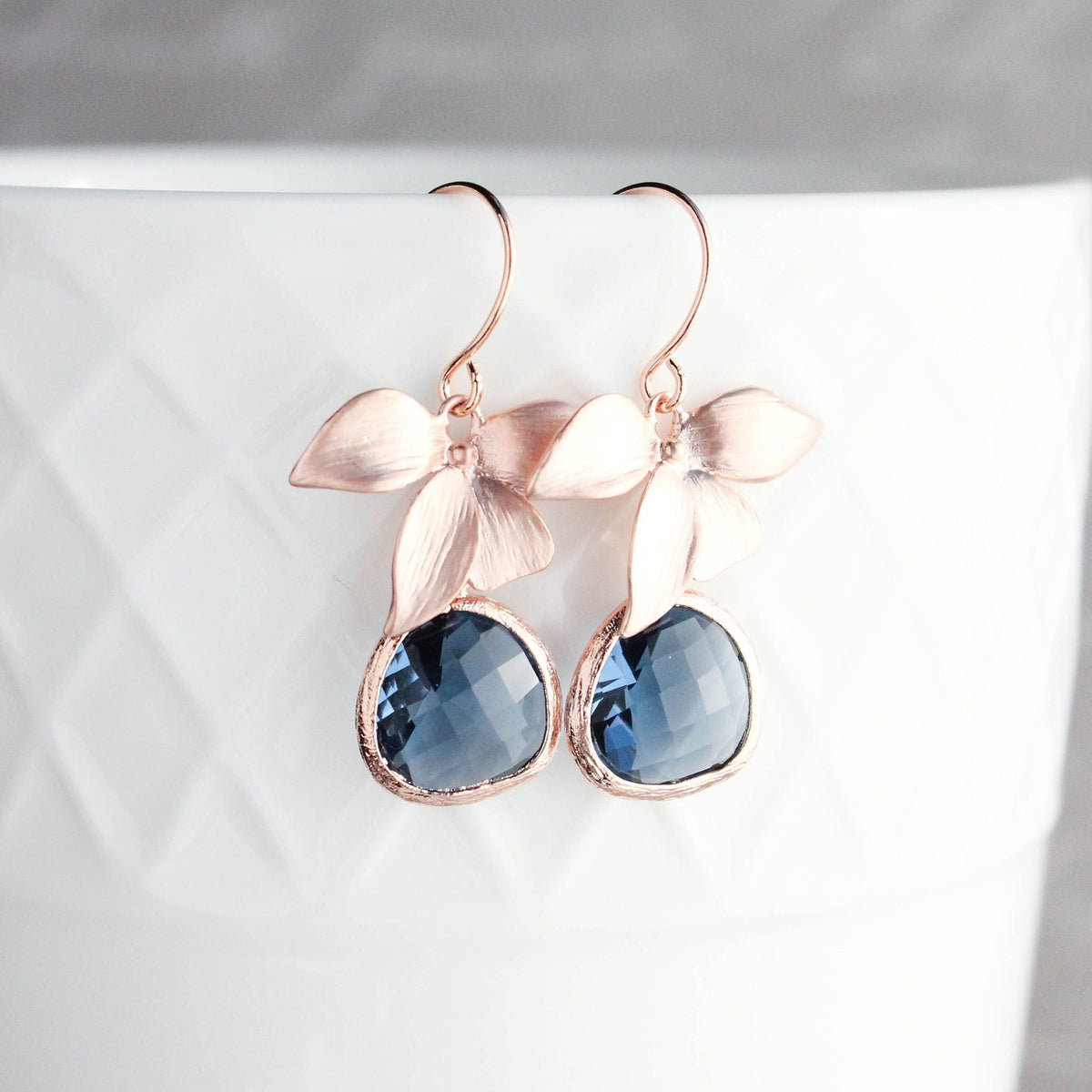 Rose gold orchid earrings with clear glass jewels in navy blue color, displayed on a white surface.