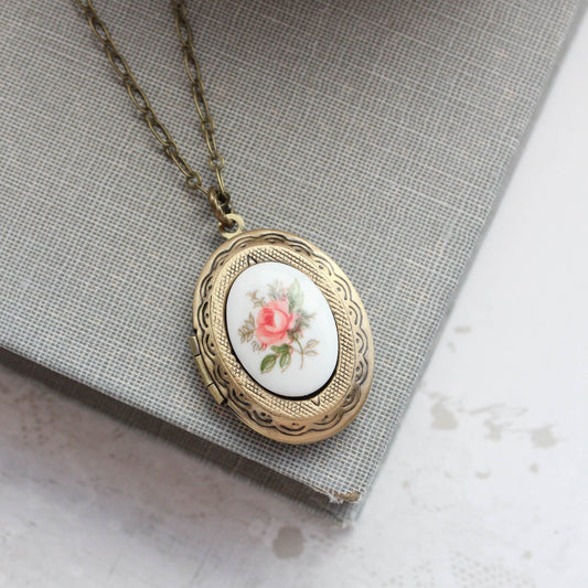 An oval vintage style locket necklace with a pink rose cameo design on the locket, suspended from an antique brass chain.
