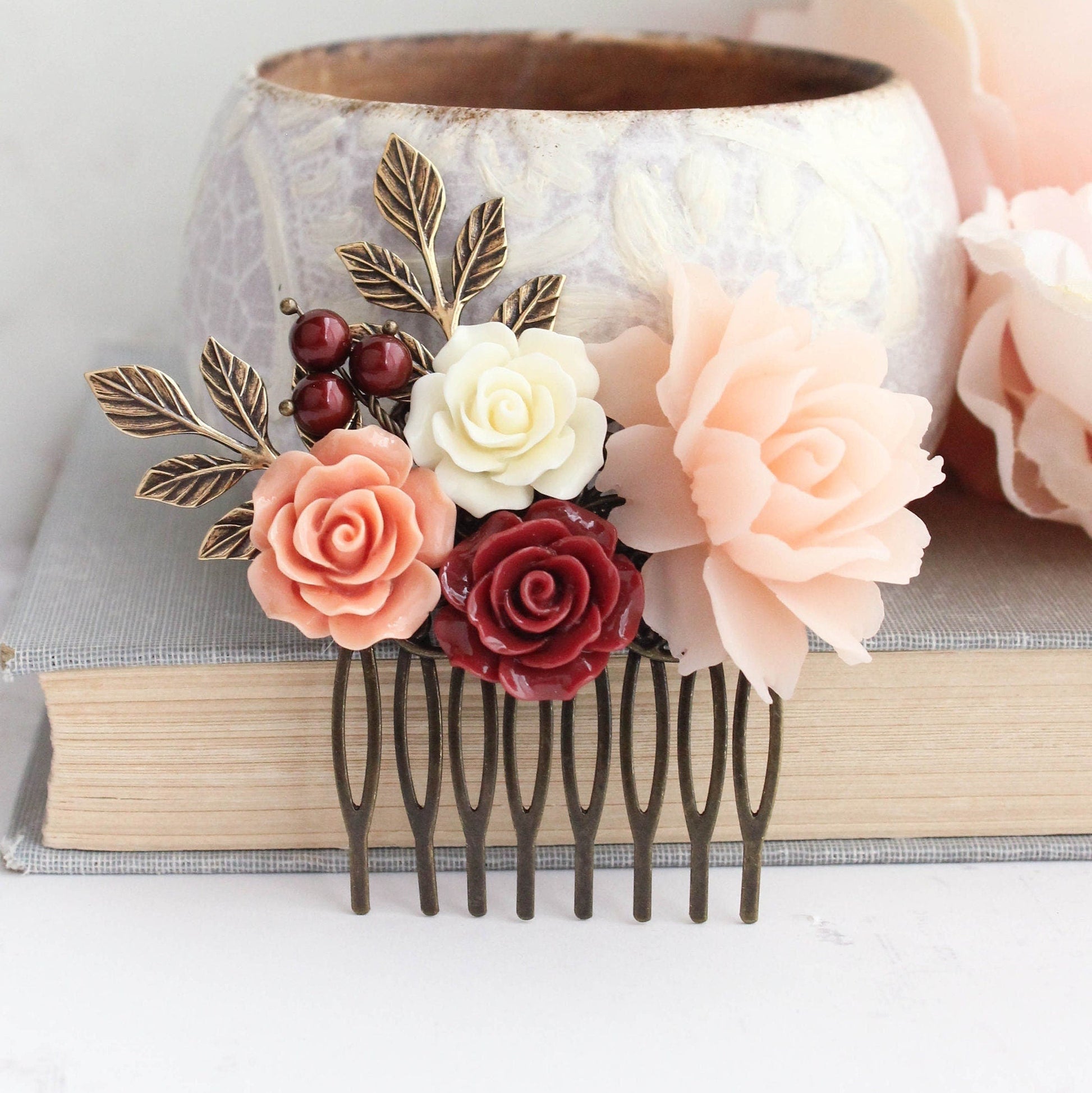 A floral hair comb featuring a mix of deep red and peach blush resin flowers, antique gold brass branches, and red pearls, displayed on a grey background.
