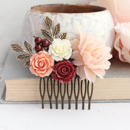 A floral hair comb featuring a mix of deep red and peach blush resin flowers, antique gold brass branches, and red pearls, displayed on a grey background.