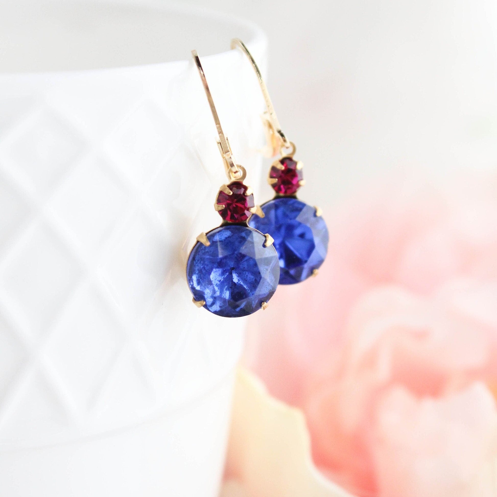 A pair of vintage style drop earrings with deep sapphire blue glass and maroon fuchsia crystal, set in gold brass prong settings.