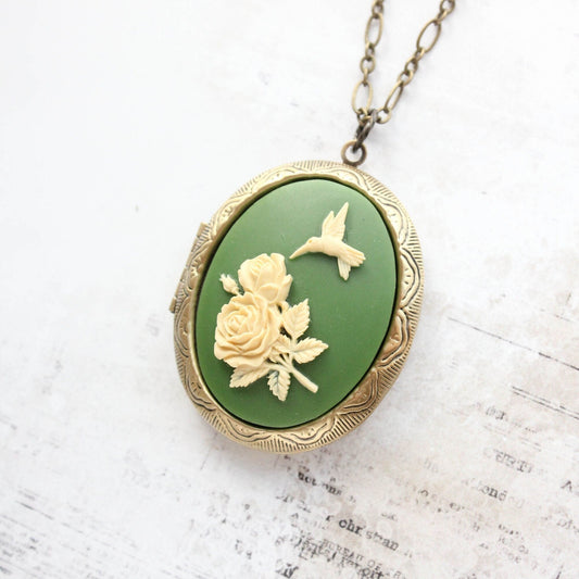 An antique brass locket pendant with a green cameo of a hummingbird and flower on a chain necklace.